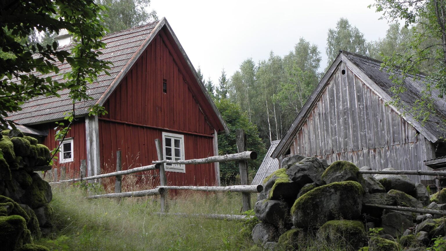 Ett rött torp till vänster och en grå lada till höger. Både husen är äldre och slitna.