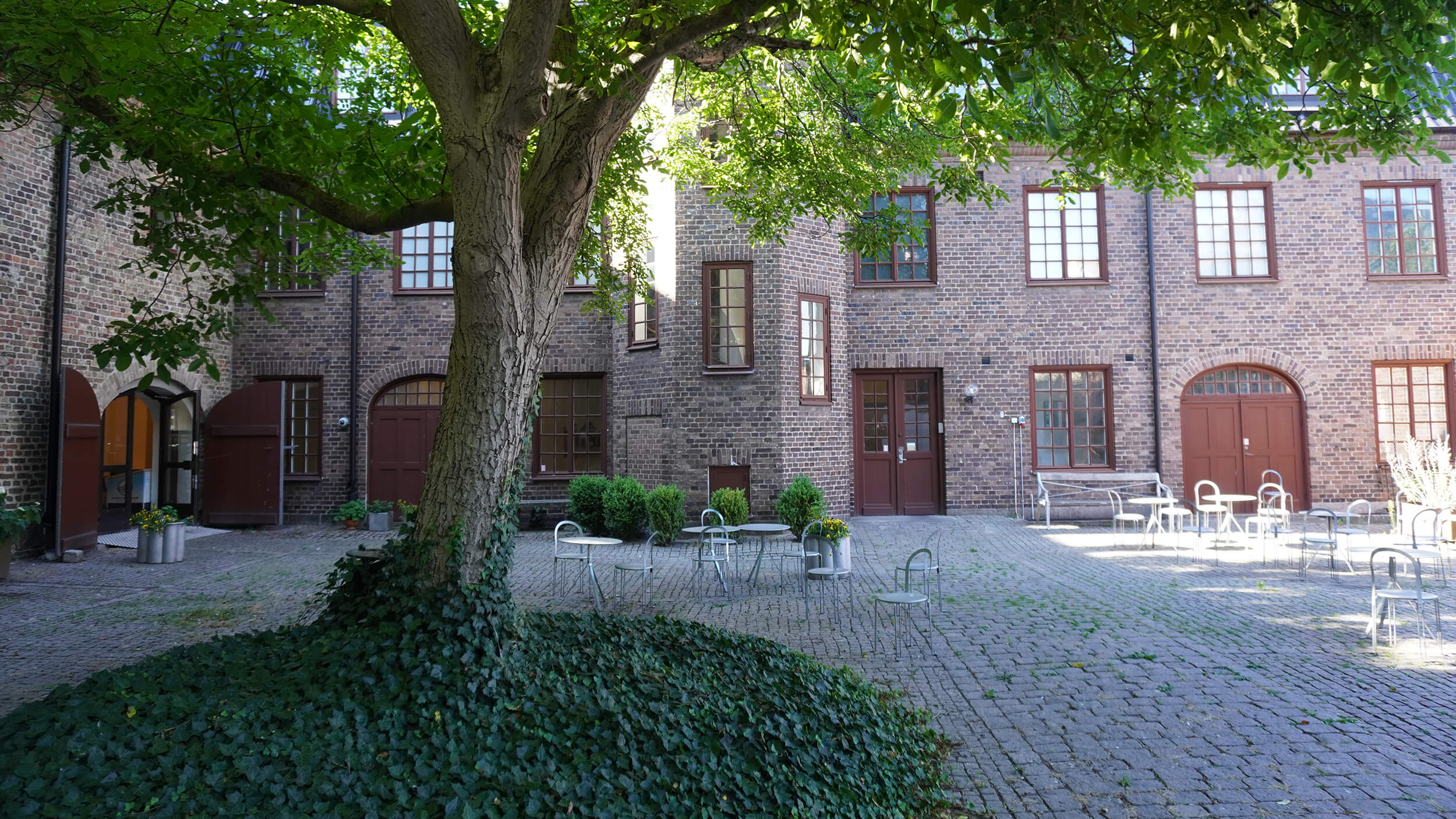 En lummig gård. I bakgrunden ett tegelhus.