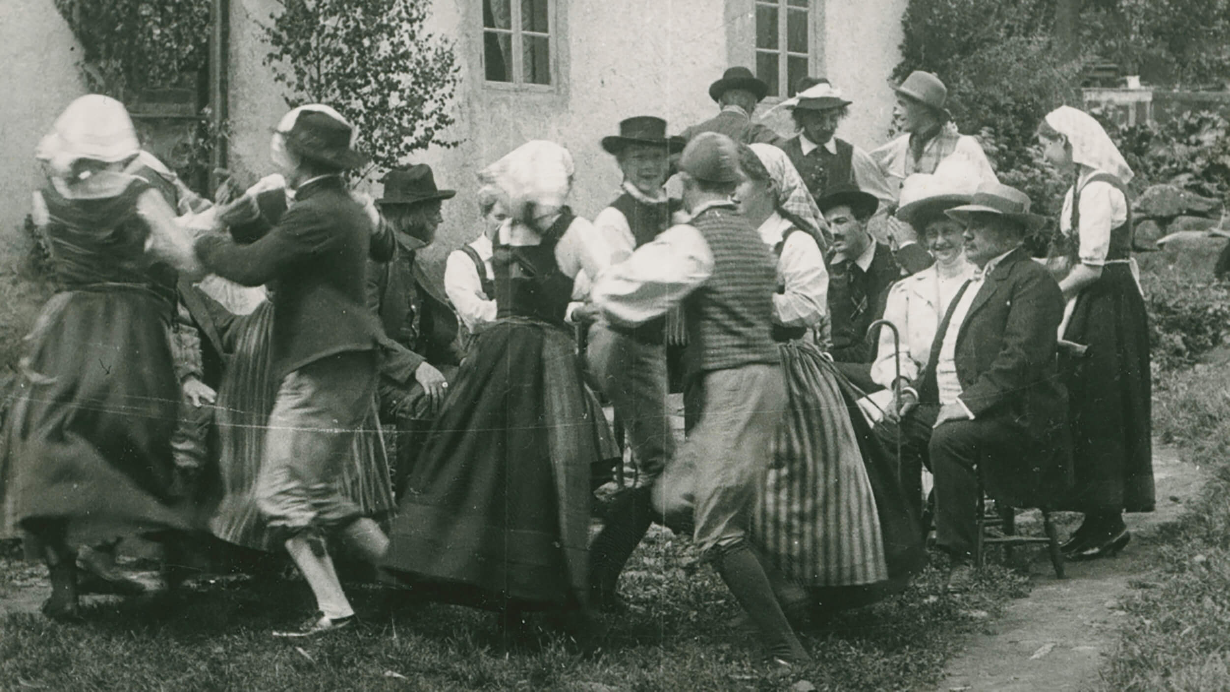 Bild från en svartvit film, folkdanslag som dansar runt.