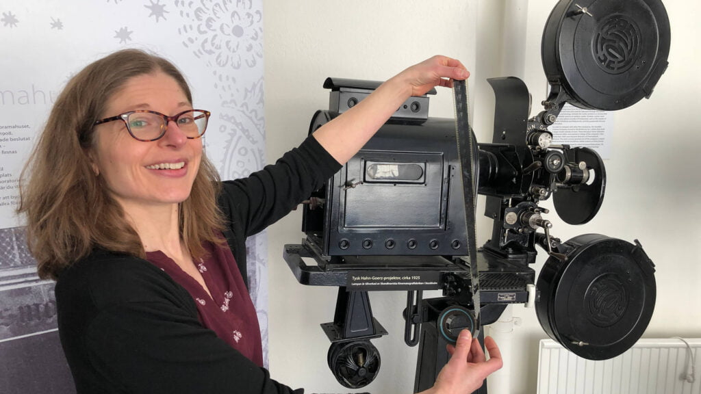En kvinna håller en filmrulle framför en gammal filmkamera.
