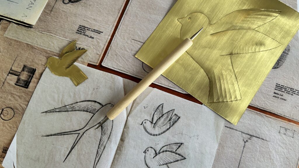 Teckningar som föreställer fåglar och en mässingsplåt på ett bord.