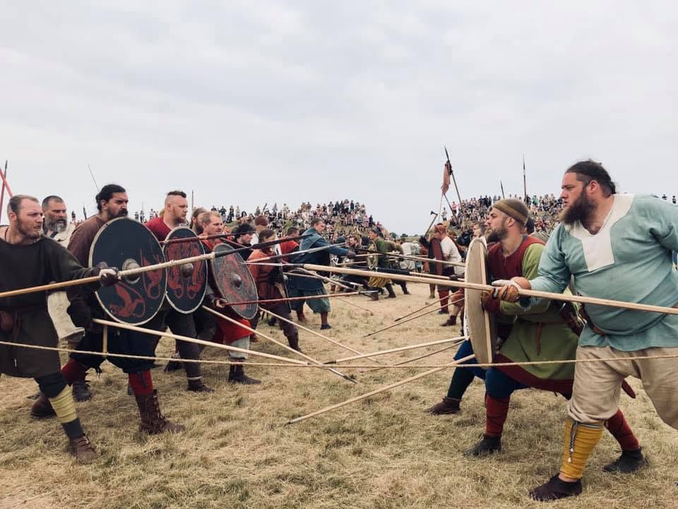 några människor återger hur ett vikingaslag skulle kunna se ut på ett gräsfält