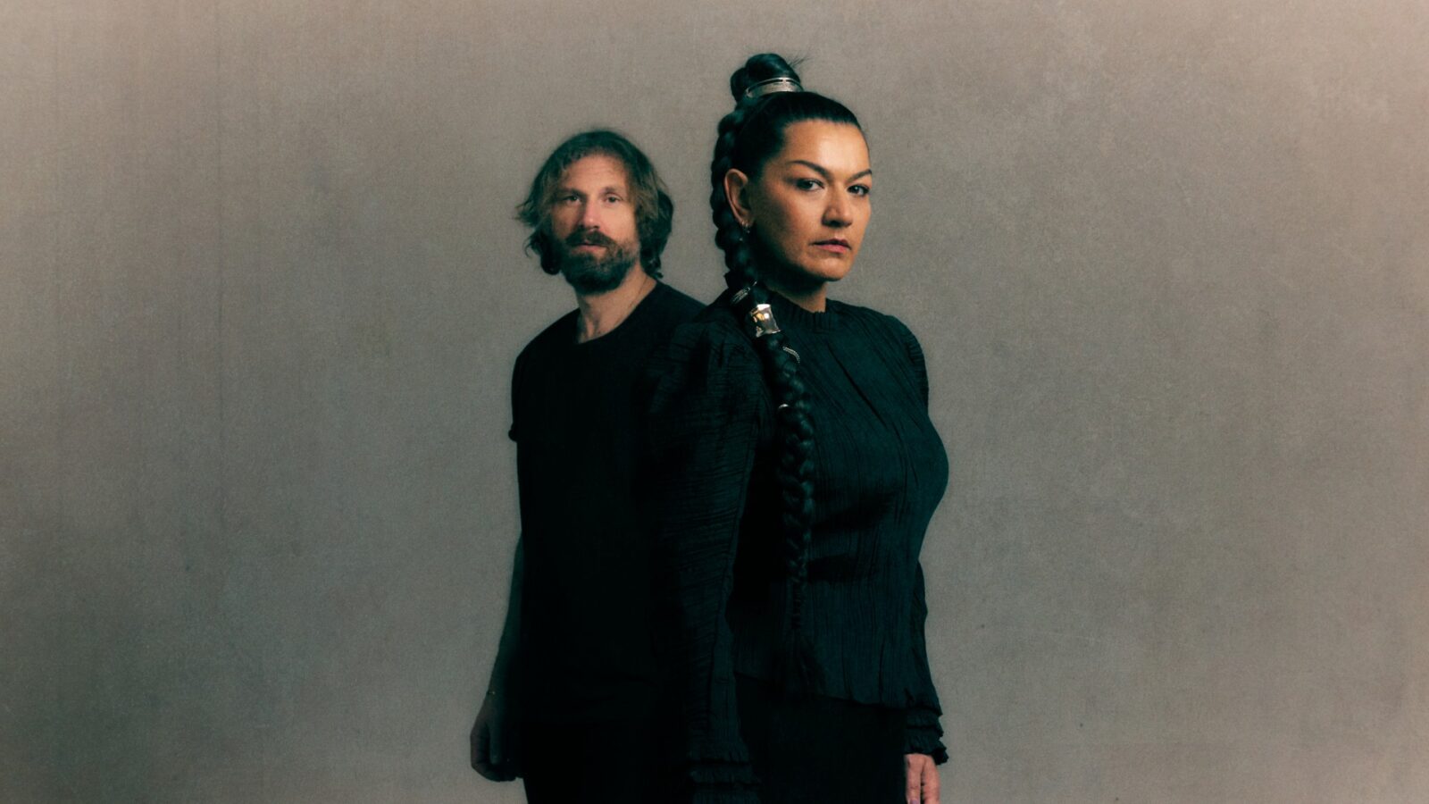 en kvinna och en man klädda i svart står mot en grå bakgrund